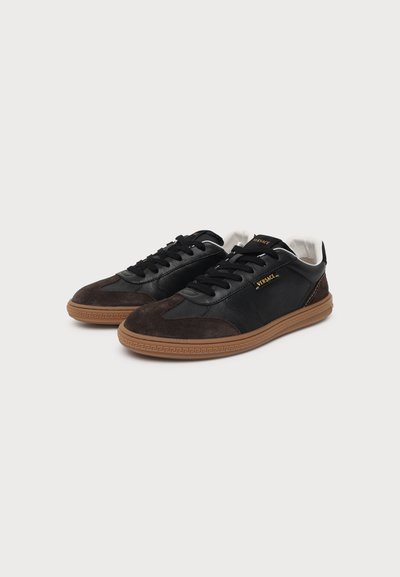 Paire de baskets basses noires et brunes avec semelles en gomme, lacets noirs et marquage Versace doré sur fond blanc.