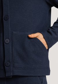 Cárdigan azul marino con una textura suave, que cuenta con botones frontales, dos bolsillos laterales y puños y dobladillo de canalé.