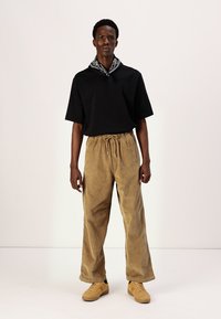 Sort kortærmet skjorte, tan corduroy bukser med elastisk talje og beige sneakers. Accessorized med et sort og hvidt bandana om halsen.