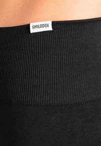 Mustat legginsit, joissa on ribbineulottu vyötärö. Edessä valkoinen "SMILODOX"-logo.