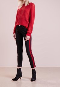 Röd stickad tröja med strukturerat mönster, svarta skinny jeans med röda sidolinjer och stövlar med spetsig tå.