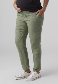 Gröna lätta byxor med elastisk midja, sidofickor och uppvikta fållar, i kombination med vita sneakers. Slät textur.