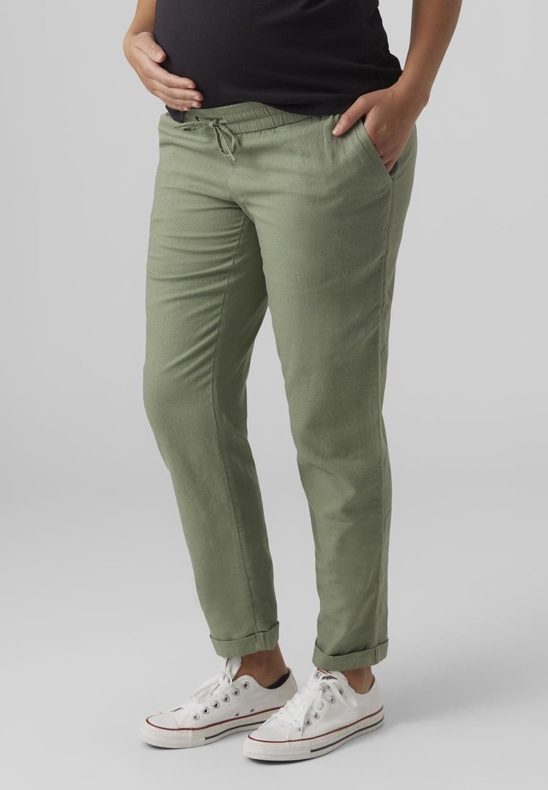 Gröna lätta byxor med elastisk midja, sidofickor och uppvikta fållar, i kombination med vita sneakers. Slät textur.