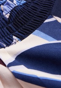 Tessuto a fantasia floreale con colori blu e crema. Presenta arricciature elastiche e una texture liscia. La composizione del tessuto appare leggera.
