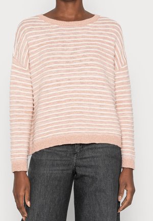 Personne portant un pull en tricot rayé rose clair et blanc à manches longues et un jean gris foncé, visible des épaules aux hanches.