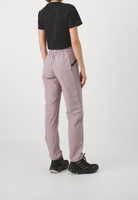 Light pink trousers with an elastic waistband, featuring black accents, side pockets, and a relaxed fit, paired with a black short-sleeve top.
