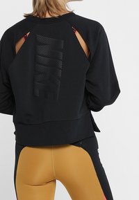 Zwarte sweatshirt met uitsparingen op de schouders, voorzien van een textuur Nike-logo in zwart op de achterkant. Het materiaal lijkt zacht en rekbaar.