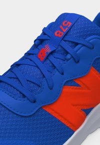 Baskets de sport bleues et oranges avec des lacets bleus, tissu en maille, et logo "NB" rouge sur la languette et le panneau latéral.