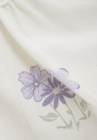 Vitt tyg med blommönster som har två lila blommor och gröna blad. Blommorna har gula mittar och en mjuk textur.