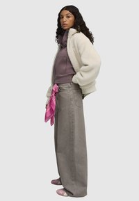 White fluffy bomber jacket over a purple zip-up hoodie, paired with high-waisted gray wide-leg jeans, accentuated by a pink bandana.