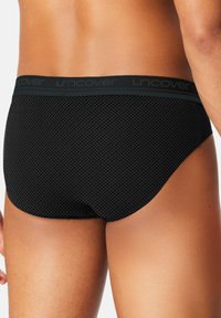 Black patterned briefs with a textured diamond design. Elastic waistband features "uncover" branding. Material is smooth and form-fitting.