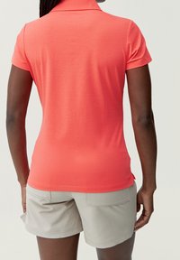 Korallfärgad pikétröja med liten krage och korta ärmar, kombinerad med ljusbeige shorts med två bakfickor. Mjuk textur.