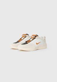Balti un bēša tenisi ar oranžu Nike zīmi un oranžām auklām, uz vienkārša gaiša fona.