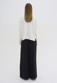 Biały oversize'owy sweter z bocznymi rozcięciami, połączony z czarnymi spodniami o szerokiej nogawce. Gładka tekstura, minimalistyczny design oraz neutralna paleta kolorów.