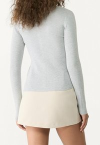 Jasnoszara prążkowana bluzka z długim rękawem o dopasowanym kroju, zestawiona z kremową plisowaną mini spódnicą, gładka faktura i minimalistyczny design.