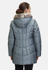 Doudoune gris clair avec une capuche en fausse fourrure, design matelassé et silhouette mi-longue, comportant des panneaux de forme rectangulaire.