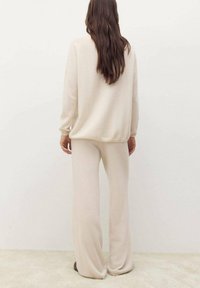 Completo in maglia beige, composto da un maglione e pantaloni, caratterizzato da una vestibilità comoda, maniche lunghe e una trama morbida, con un design semplice e sobrio.