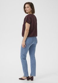 Kurzärmliges, burgunderfarbenes Musteroberteil mit lockerer Passform, kombiniert mit hellblauen, geraden Jeans und dunklen, Absatzmules, von hinten betrachtet.
