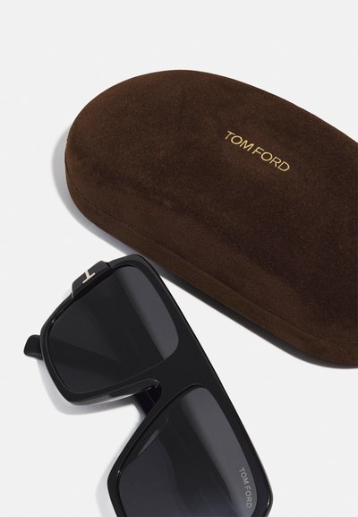 Occhiali da sole neri con una finitura liscia, caratterizzati da montature spesse, accompagnati da una custodia in suede marrone con il testo in oro "TOM FORD" in rilievo.