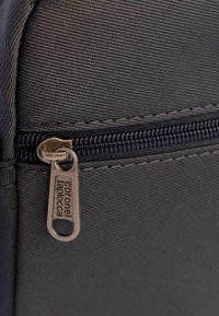 Funda de tela negra con una superficie texturizada, con una cremallera de metal y un tirador etiquetado "Coronel Taplocca".