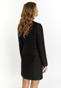 Abito in blazer nero con texture, maniche lunghe, silhouette aderente e orlo leggermente svasato, con un motivo geometrico.
