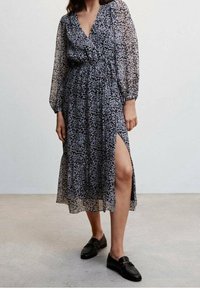 Zwart bloemen midi-jurk met lange, opgezette mouwen, v-hals en een hoge split. Gemaakt van lichtgewicht, doorschijnende stof met kleine bloempatronen.