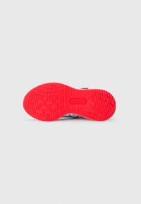 Semelle de sneaker rouge vif avec un motif de semelle détaillé et texturé, présentée sur un fond gris clair uni.