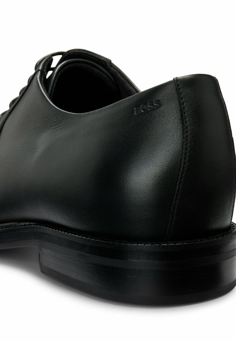 Zwarte leren dresschoenen met een gladde textuur en een ronde vorm. Bevat subtiele branding nabij de hak en een gelaagde zwarte zool.