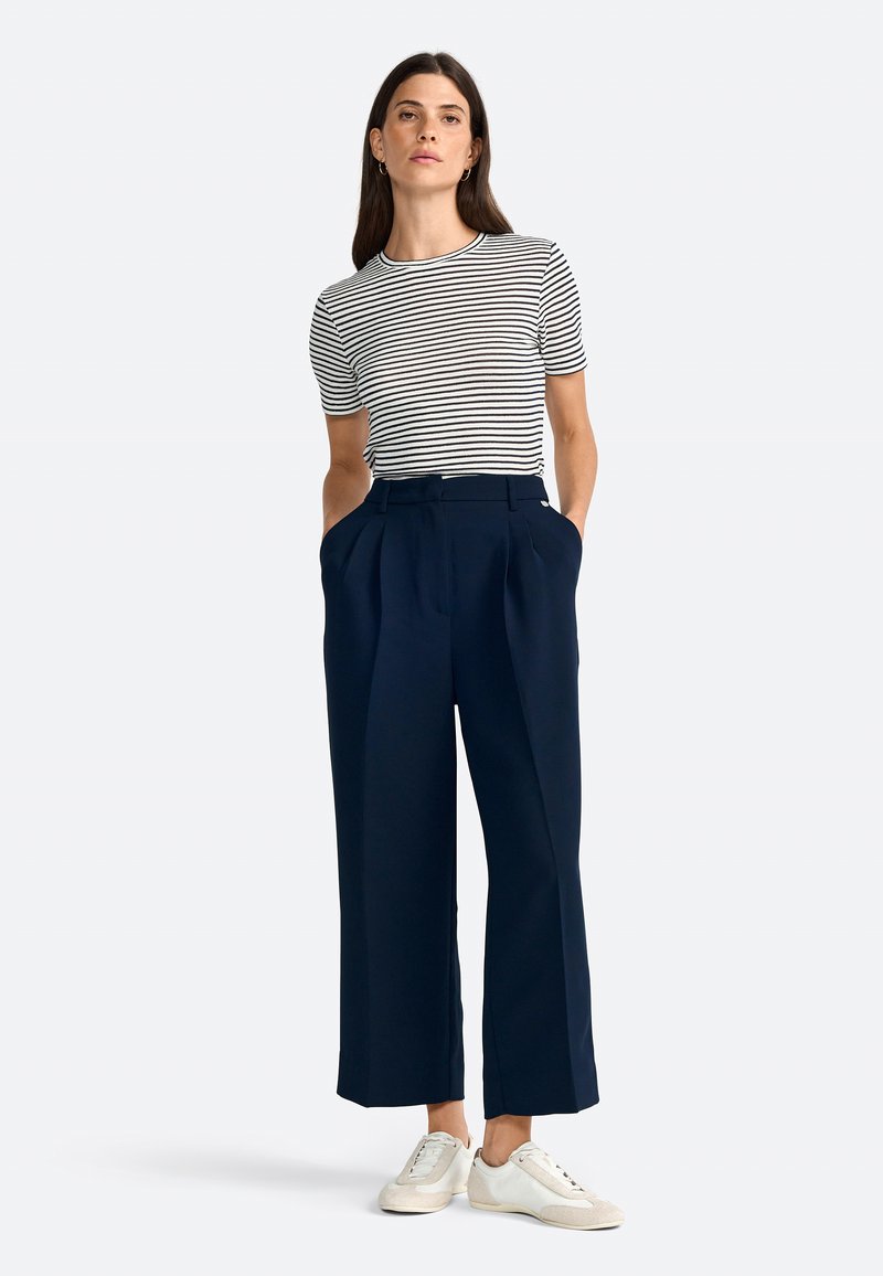 Striped short-sleeve top with round neckline, paired with navy wide-leg trousers featuring side pockets, complemented by white sneakers.