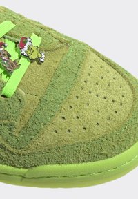 Zelený texturovaný špička tenisky s jasnými tkaničkami, na kterých jsou přívěsky Grinche a psa s čepicemi Santa.
