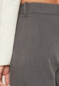 Pantaloni grigi su misura realizzati in tessuto testurizzato e con un sottile motivo verticale. Presentano una vita slim con passanti per la cintura, mostrati insieme a una manica bianca a coste.
