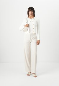White ribbed cardigan with gold buttons, paired with cream wide-leg trousers and beige open-toe heeled mules featuring a logo accent.