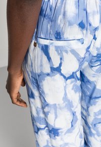 Pantalones ligeros y estampados en azul y blanco, con un sutil efecto de tie-dye, que presentan un detalle de bolsillo bordado y una textura suave.