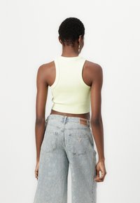 Ljusgrön ribbad ärmlös crop top som matchas med blekblå vida jeans med en slitna finish och märkesläderlappar på baksidan.