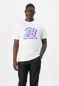 Hvid bomulds t-shirt med et stort pink og blåt "New Balance" logo på forsiden. Korte ærmer og rund hals design.