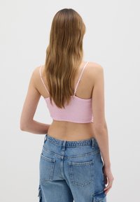 Top corto rosa chiaro con texture arricciata e spalline sottili, abbinato a pantaloni denim blu a vita alta con tasche posteriori.