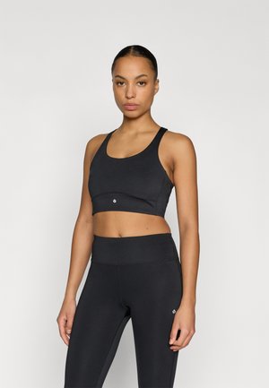 Top court de sport noir avec larges bretelles et panneaux en mesh, associé à des leggings noirs taille haute avec un petit logo. Texture lisse.