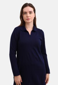 Navy long-sleeve polo dress with a collar, featuring a slim fit and subtle stitching detail along the front. Soft-textured fabric.