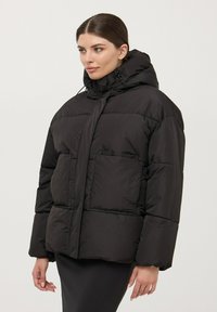 Giacca a vento nera con cappuccio, caratterizzata da un design quadrato, due tasche frontali e una texture liscia e lucida. Finestra di regolazione al collo.