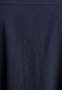 Tumši zils audums ar smalku dimanta rakstu un vieglām vertikālām krokām, attēlojot detaļas pinuma rakstu un nelielu ēnojumu.