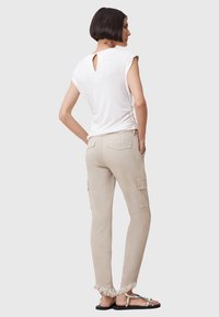 Top blanco de manga corta con detalle de abertura en la espalda, combinado con pantalones cargo beige que cuentan con bolsillos laterales y dobladillos desflecados. Sandalias planas.