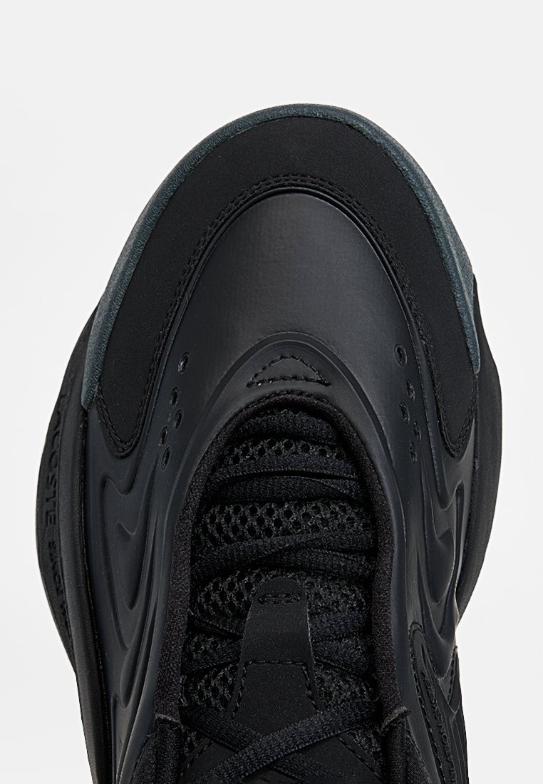 Black sneaker featuring a smooth leather upper and textured mesh detailing. Sleek design with a rounded toe and cushioned sole.