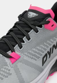 Γκρίζο αθλητικό παπούτσι με υφασμάτινο επάνω μέρος, μαύρους κορδόνια, ροζ λεπτομέρειες και ένα χαρακτηριστικό λογότυπο στην γλώσσα και στο πλάι.