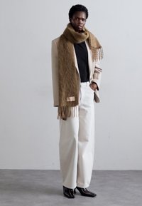 Beige blazer, sort t-shirt og hvide high-waisted bukser. Brun tørklæde med frynser. Sorte spidse sko. Minimalistisk design og neutrale farver.