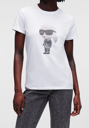 Biała koszulka z grafiką z czarnych i białych kryształków przedstawiającą postać w okularach przeciwsłonecznych i garniturze. Krótkie rękawy, klasyczny krój.