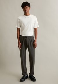Men's white cotton t-shirt with short sleeves, paired with gray trousers featuring a belt, and black shoes, set against a neutral background.