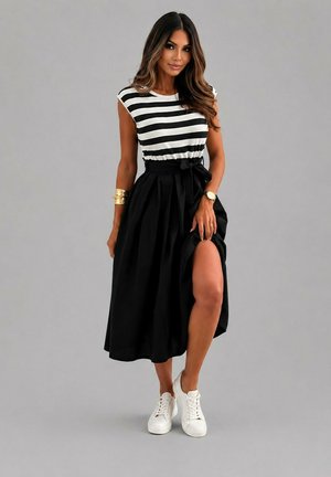 Femme portant un haut rayé noir et blanc et une jupe noire taille haute avec une fente devant, associée à des baskets blanches et des accessoires dorés.