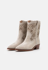 Light gray suede ankle boots with floral cut-out designs and a pointed toe. Features a stacked wooden heel for stability.