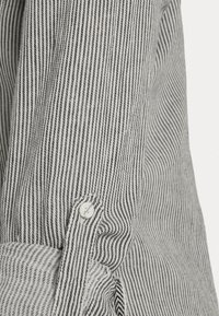 Gestreifter Hemdsärmel in Schwarz und Weiß mit feinen vertikalen Streifen, einem Knopfverschluss und einer weichen Textur.