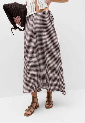 Woman wearing a high-waisted, brown and white checkered midi skirt, brown gladiator sandals, holding a dark woven clutch bag.